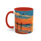 A ceramic coffee mug with a red handle and interior, featuring a colorful printed graphic of a beach sunset with seagulls, a pier, and ocean waves.